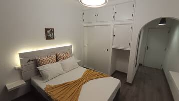 Ein Schlafzimmer mit Bett, Nachttisch, Kleiderschrank und einem anliegenden Flur.