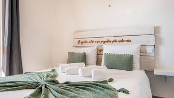 Een net opgemaakt bed met witte lakens en een groen gebreide deken, kussens met groene kwastjes, en een houten hoofdbord met een decoratief plaquette.