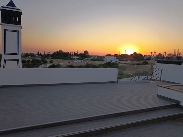 A rooftop terrace with a view of a sunset over a residential area.