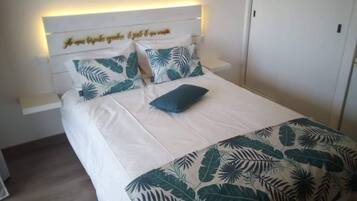 Una cama con cabecera, ropa de cama blanca y estampado de hojas tropicales.