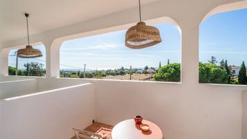 A balcony with a table and chairs, a hanging light fixture, and a view of the landscape.