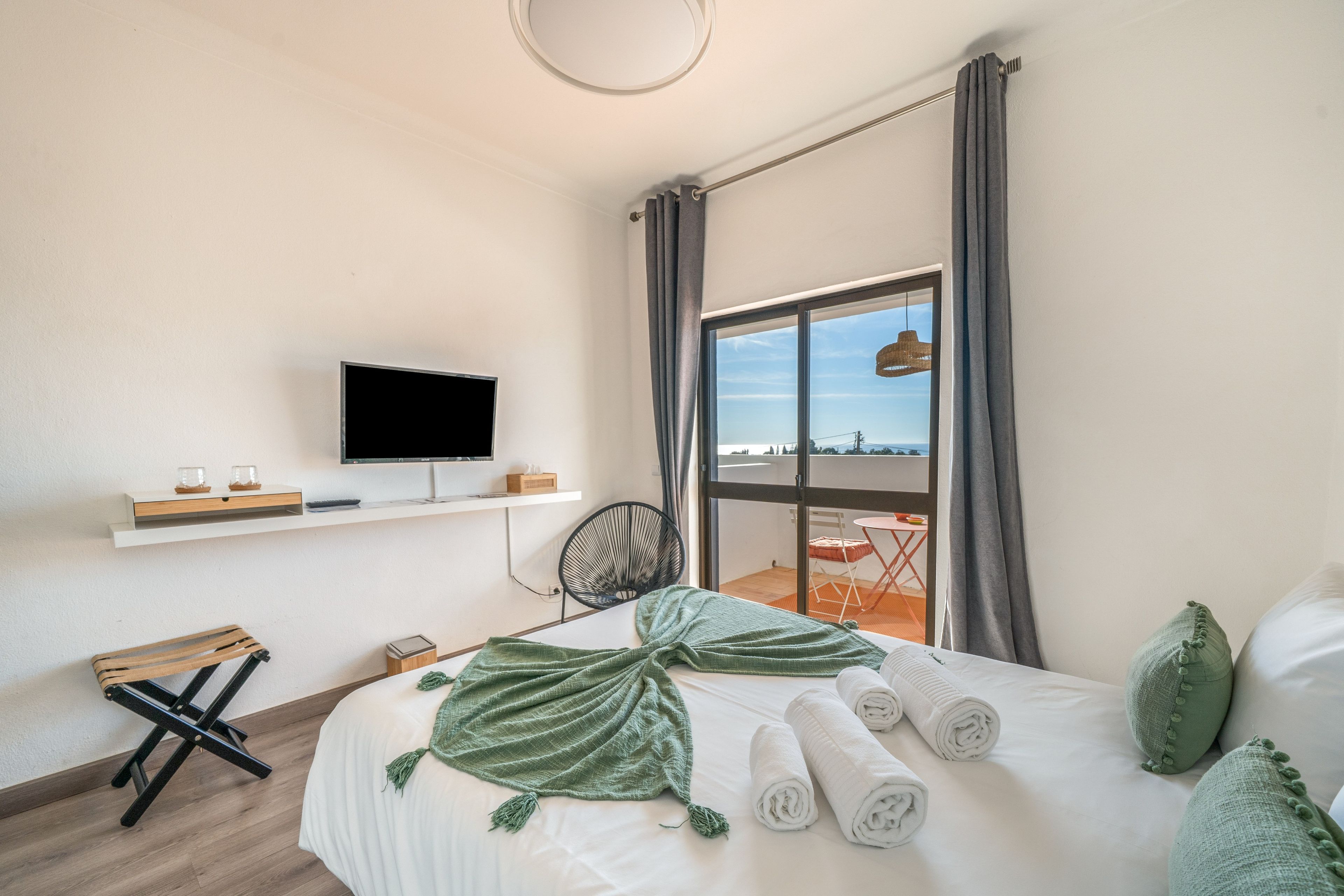 Ett hotellrum med en säng, en tv, ett fönster med gardiner och utsikt över omgivningen.