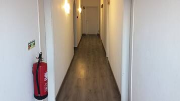 Ein Flur mit an der Wand montiertem Feuerlöscher, einer Tür mit einer Nummer und einer Leuchte.