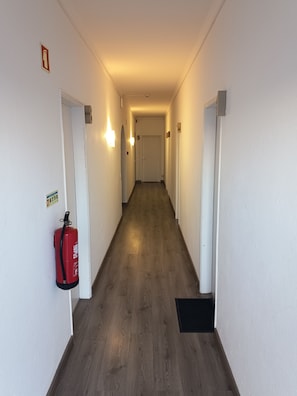 A hallway with a fire extinguisher mounted on the wall, a door with a number, and a light fixture.