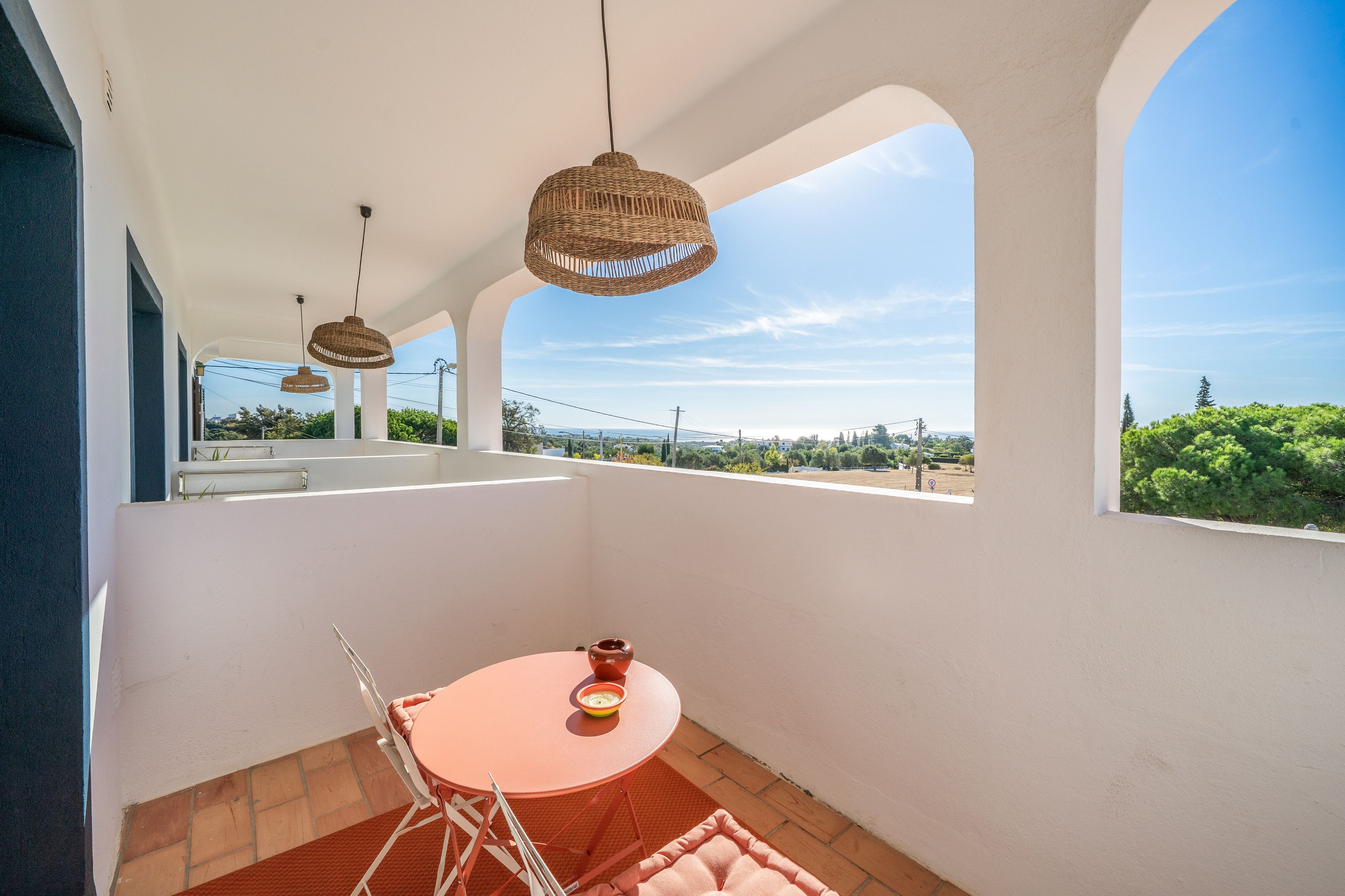 Ein Balkon mit einem runden Tisch, zwei Korbschwinglampen und Blick auf die Landschaft.
