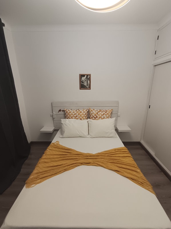 A bedroom with a bed, pillows, a bedside table, a wall-mounted picture, and a window.