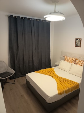 A bedroom with a bed, a chair, a curtain, and a ceiling light.
