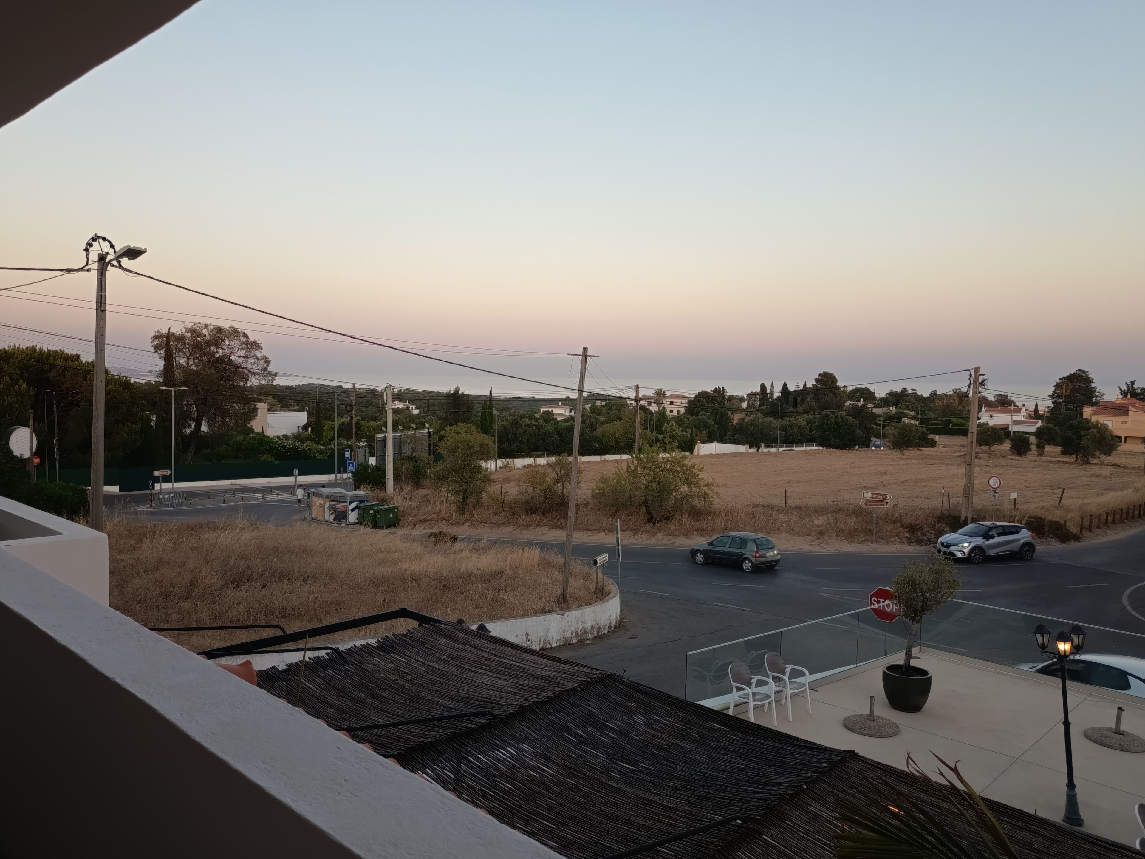Une vue depuis un balcon donnant sur une rue, avec des voitures, un panneau de signalisation et un ciel dégagé.