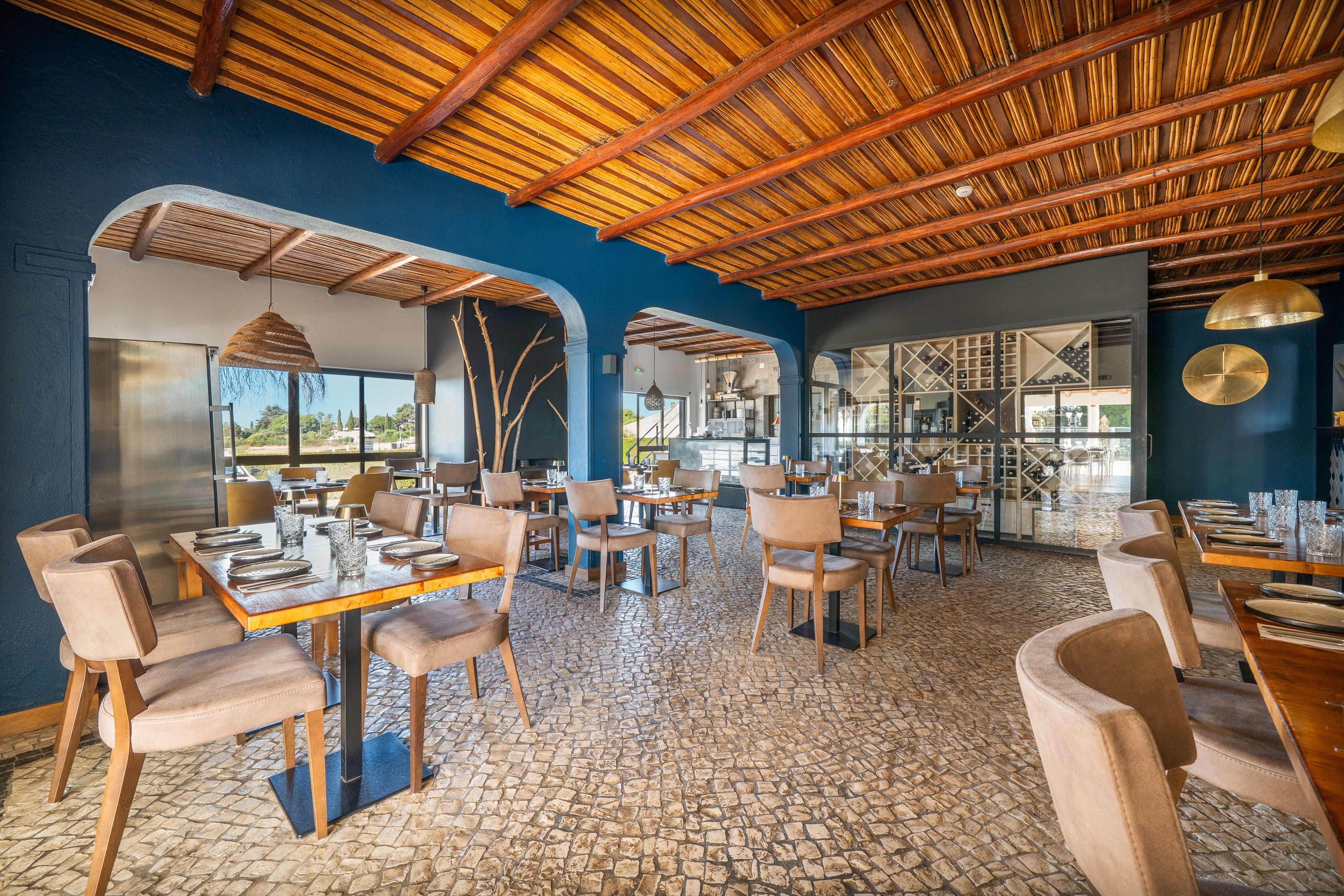 Een restaurant met een rustiek interieur, met zichtbare houten balken, stenen vloeren en uitzicht door grote ramen.