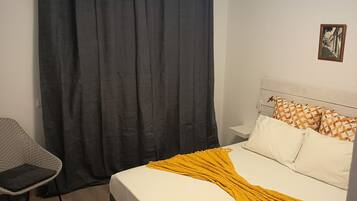 Ein Schlafzimmer mit Bett, Sessel, Vorhang und Deckenleuchte.