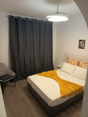 A bedroom with a bed, a chair, a curtain, and a ceiling light.