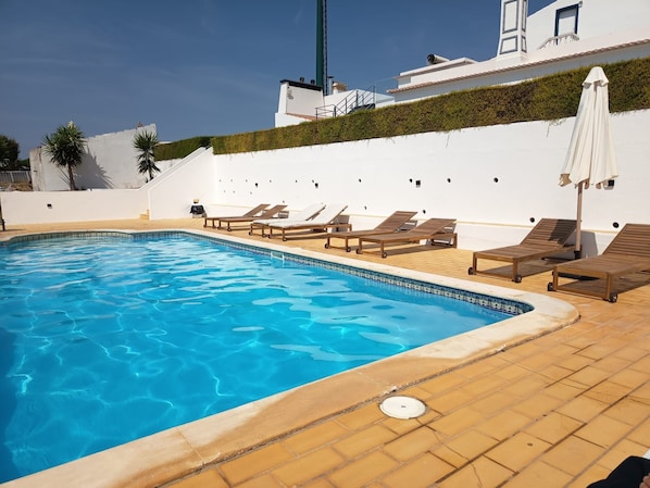 A swimming pool with lounge chairs and a white wall with a green hedge.