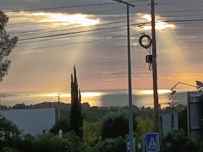 A sunset over a body of water with power lines and a pedestrian crossing sign in the foreground.