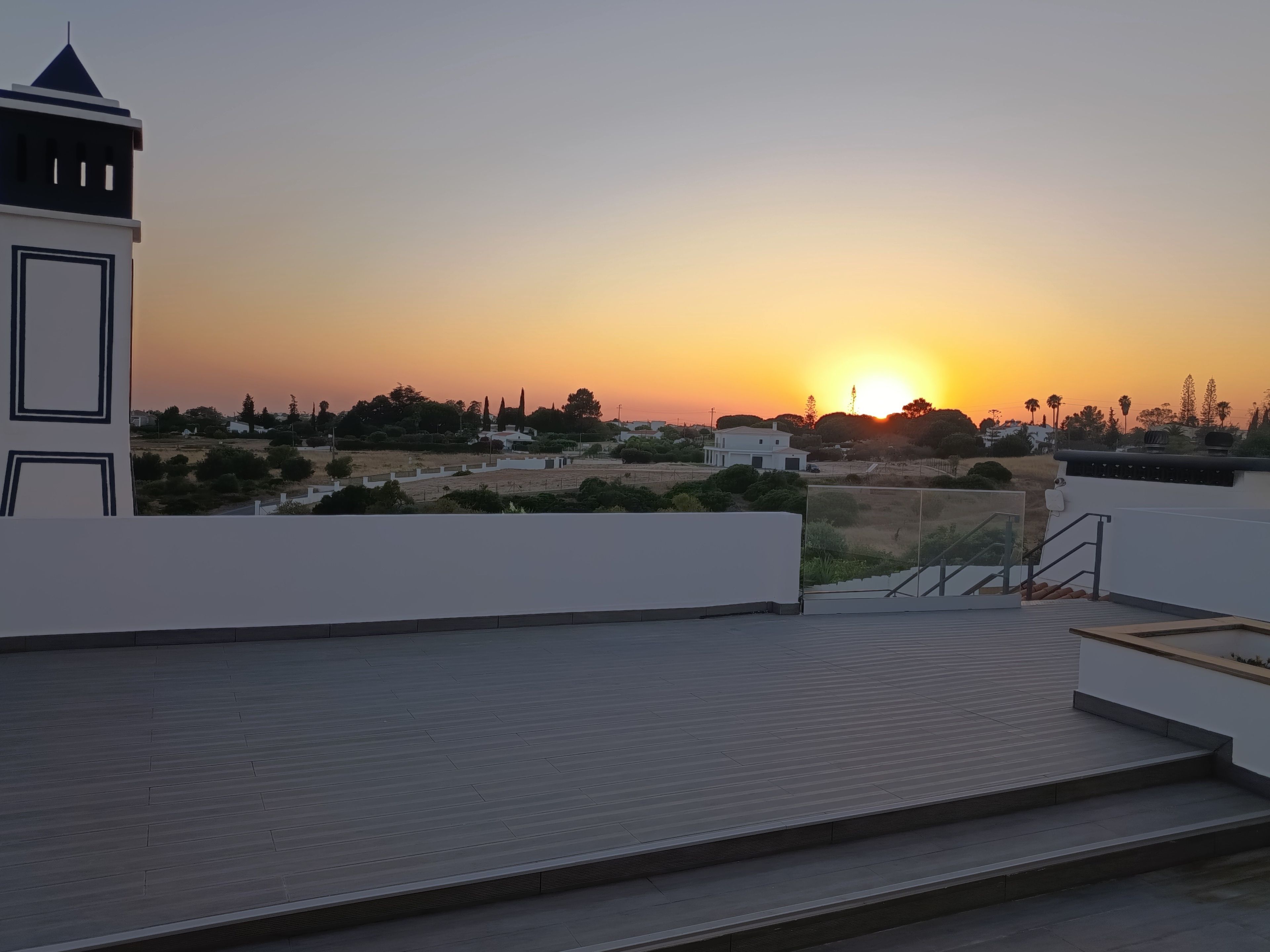 Une terrasse sur le toit offrant une vue sur le coucher de soleil au-dessus d’un quartier résidentiel.