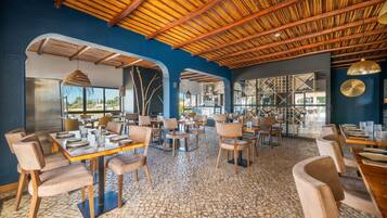 Een restaurant met een rustiek interieur, met zichtbare houten balken, stenen vloeren en uitzicht door grote ramen.