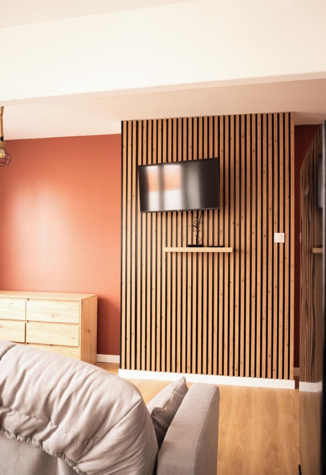 A modern bedroom with a TV mounted on a wooden slat wall, a wooden dresser, and a sofa.