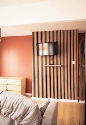 A modern bedroom with a TV mounted on a wooden slat wall, a wooden dresser, and a sofa. - Apartment (Bourbourg)