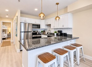 A modern kitchen with stainless steel appliances, a granite countertop, and white cabinetry. - Modern Renovated Condo - 90 Steps to Beach - Indoor Pool - OCMD (Ocean City)