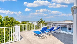 A balcony with a white railing, blue lounge chairs, and a view of buildings and trees. - Modern Renovated Condo - 90 Steps to Beach - Indoor Pool - OCMD (Ocean City)