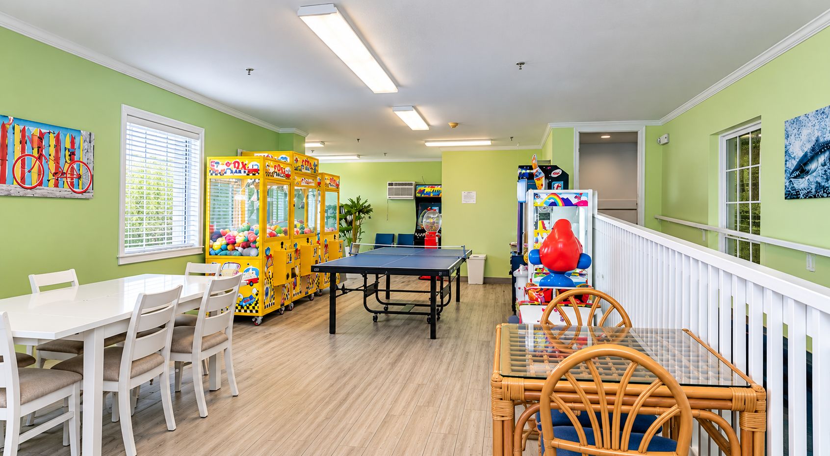 A room with a ping pong table, white chairs, a dining table, and colorful play structures.