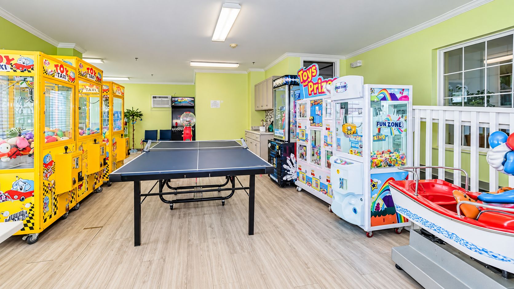 A brightly lit indoor play area with a ping pong table, various toy vending machines, and a small boat ride.