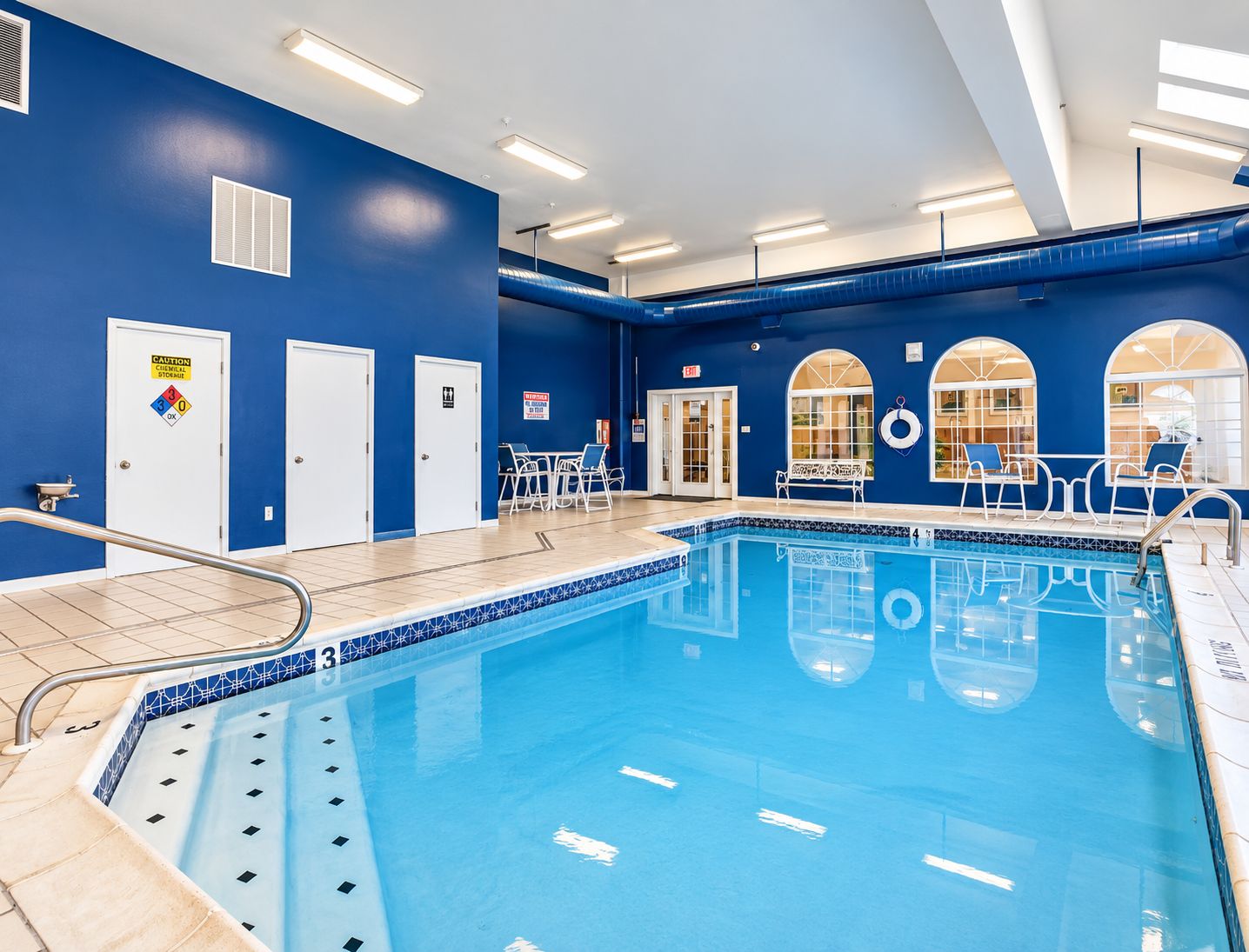 Ein Hallenbad mit deutlichen Fahrbahnmarkierungen, Sicherheitszeichen und einem Rettungsschwimmerstuhl.