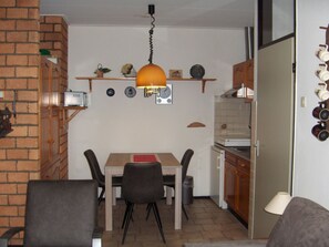 A compact kitchen with a dining table and chairs, a hanging light fixture, and a refrigerator. - Holiday Apartment With 2 Bedrooms (De Koog)