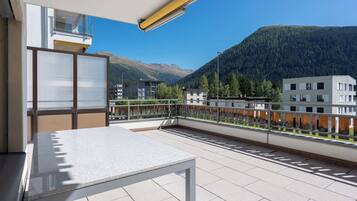 A balcony with a table and chairs, overlooking a mountainous landscape with buildings in the background.