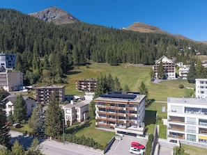 Ein modernes Hotel mit mehreren Etagen, einem Parkplatz und Blick auf eine Berglandschaft.