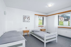 Ein Schlafzimmer mit zwei Einzelbetten, einem Nachttisch mit Lampe, einem Wandbild und einem Fenster mit Vorhängen.