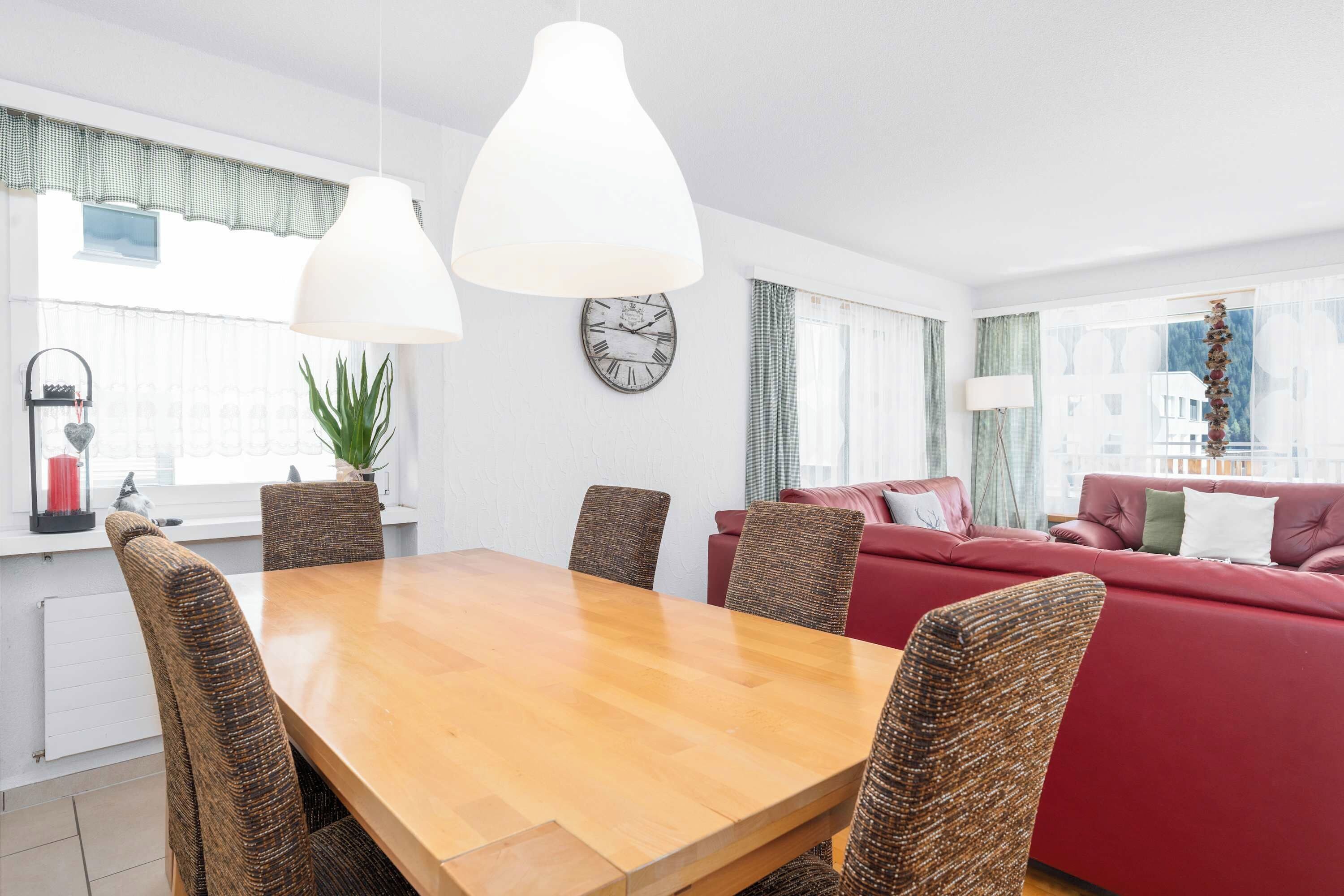 Un salon moderne avec une table à manger en bois, des chaises en osier, un canapé rouge et une grande fenêtre avec des rideaux.