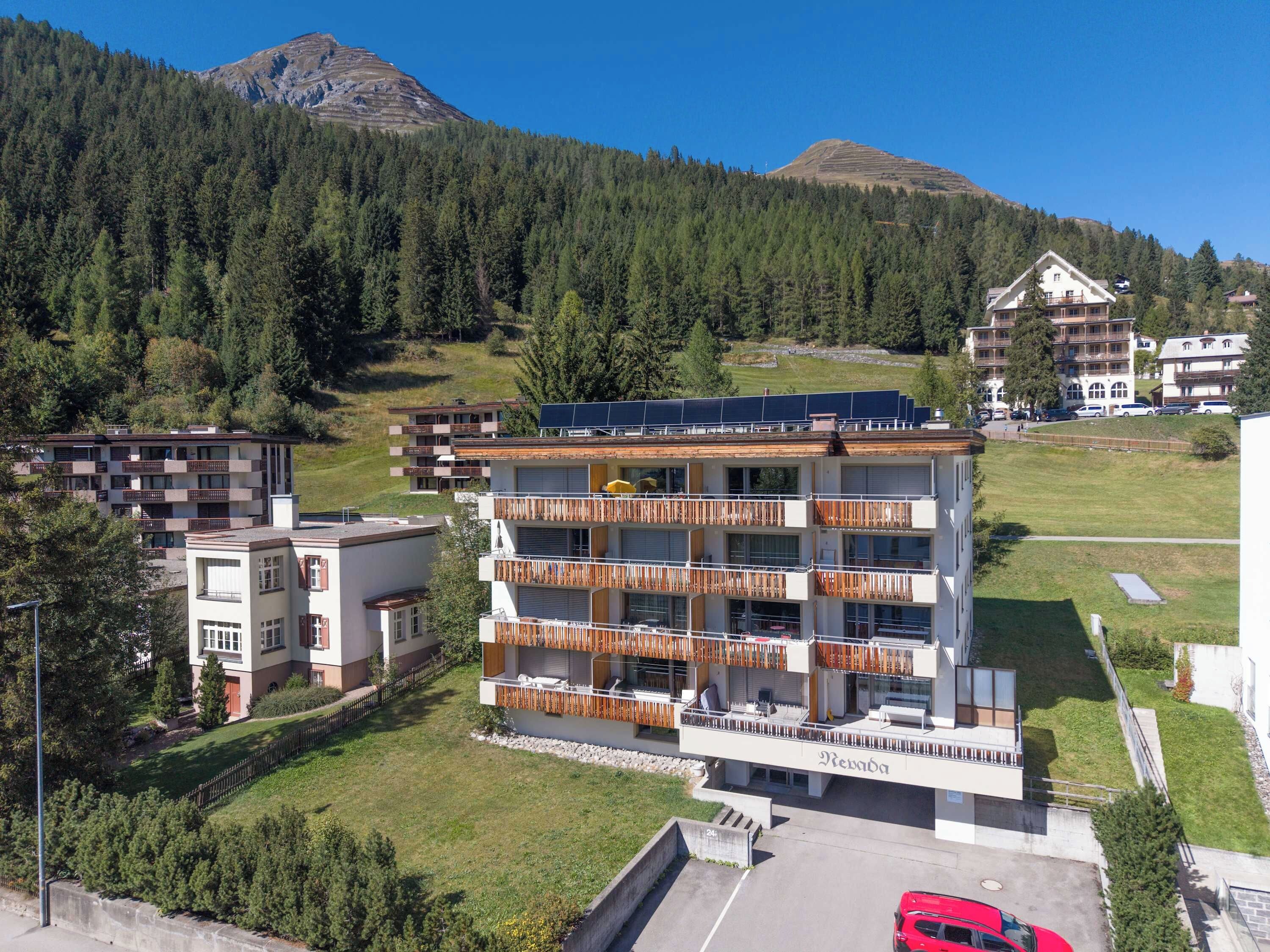 Un edificio de varios pisos con balcones, paneles solares y una zona de estacionamiento.
