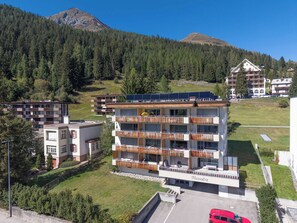 A multi-story building with balconies, solar panels, and a parking area.