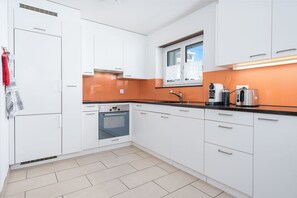 Eine moderne Küche mit weißen Schränken, einem Backofen, einer Spüle und einem Fenster über der Arbeitsplatte.