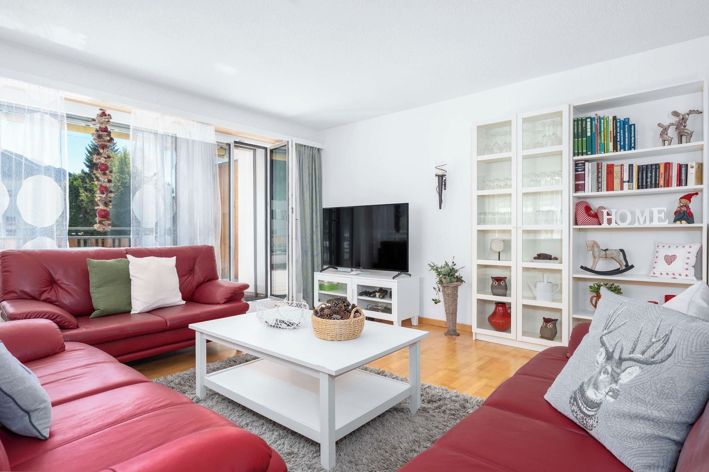 Una sala de estar moderna con un sofá rojo, una mesa de centro blanca y una estantería llena de libros y objetos decorativos.