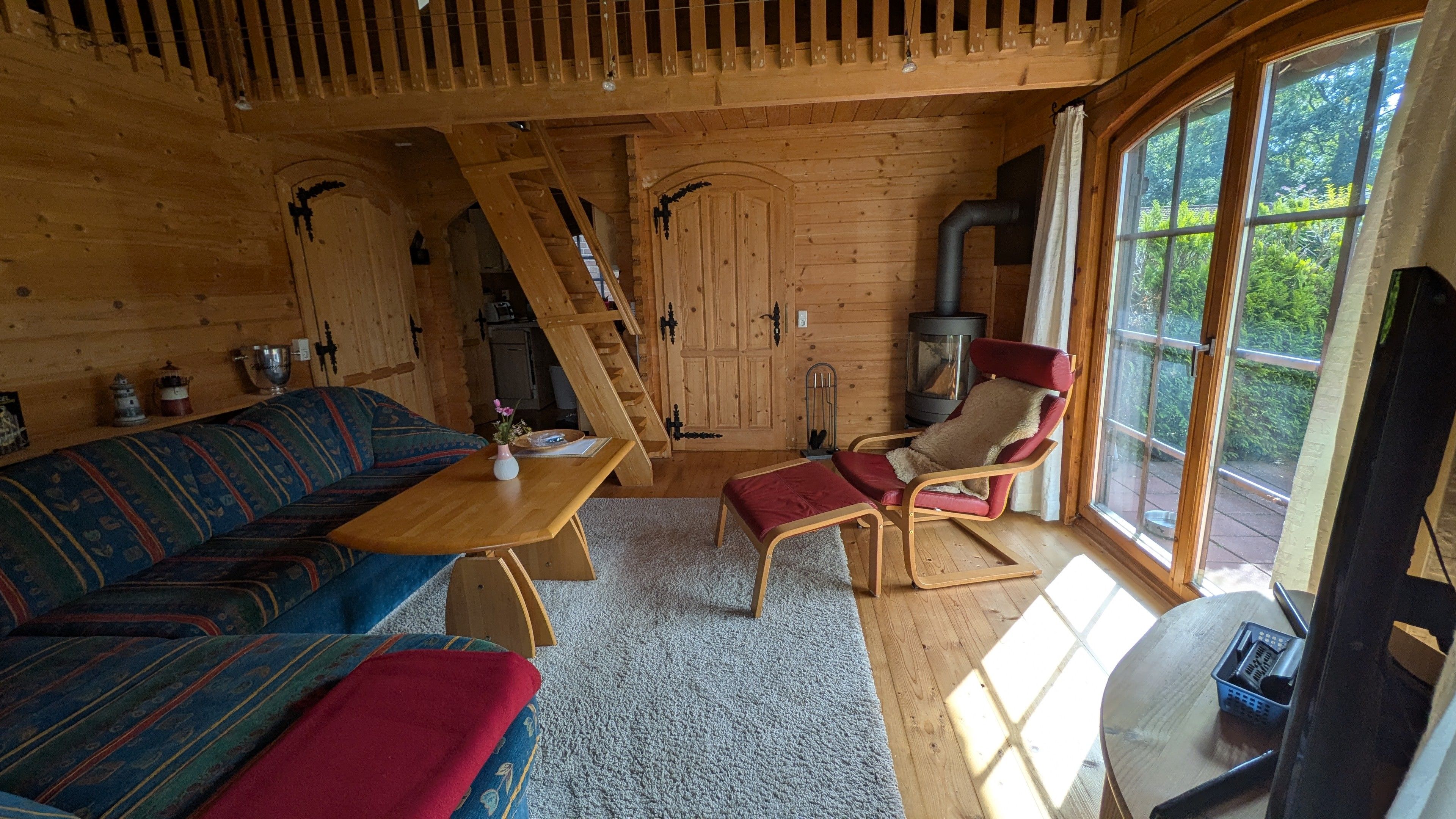 Ein gemütliches Blockhaus-Interieur mit Holzausstattung, einer Couch, einem Tisch, einem Stuhl und einem großen Fenster.