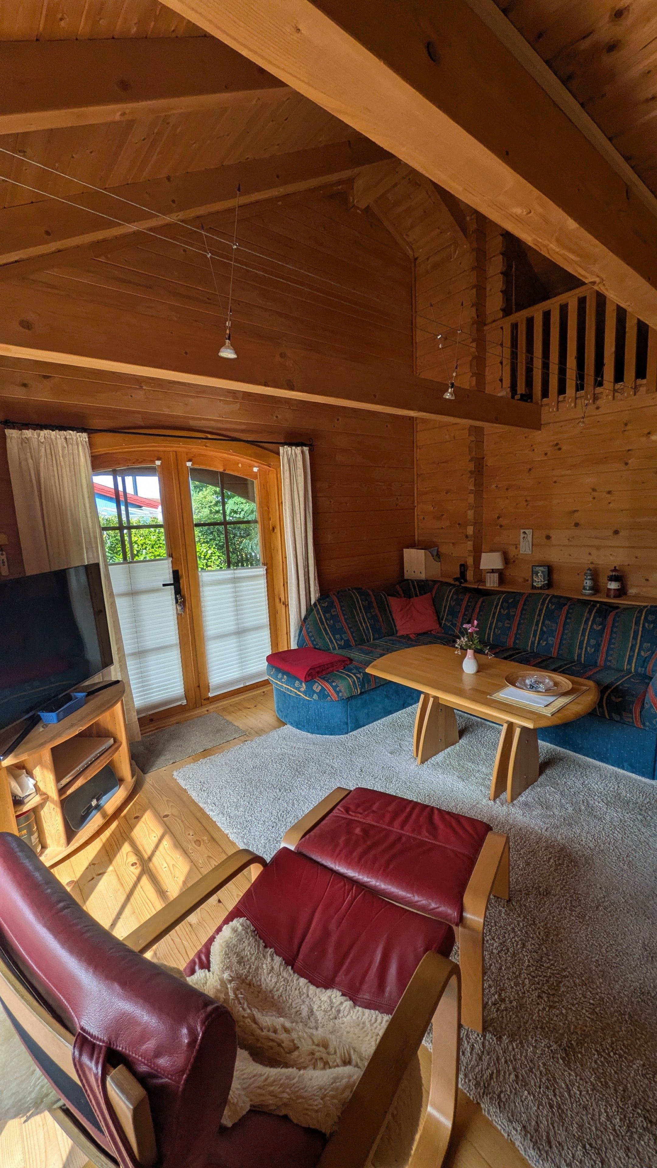 A cozy cabin interior with a wooden ceiling, a sofa set, a television, and a dining table.