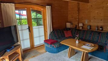 A cozy cabin interior with a wooden ceiling, a sofa set, a television, and a dining table.