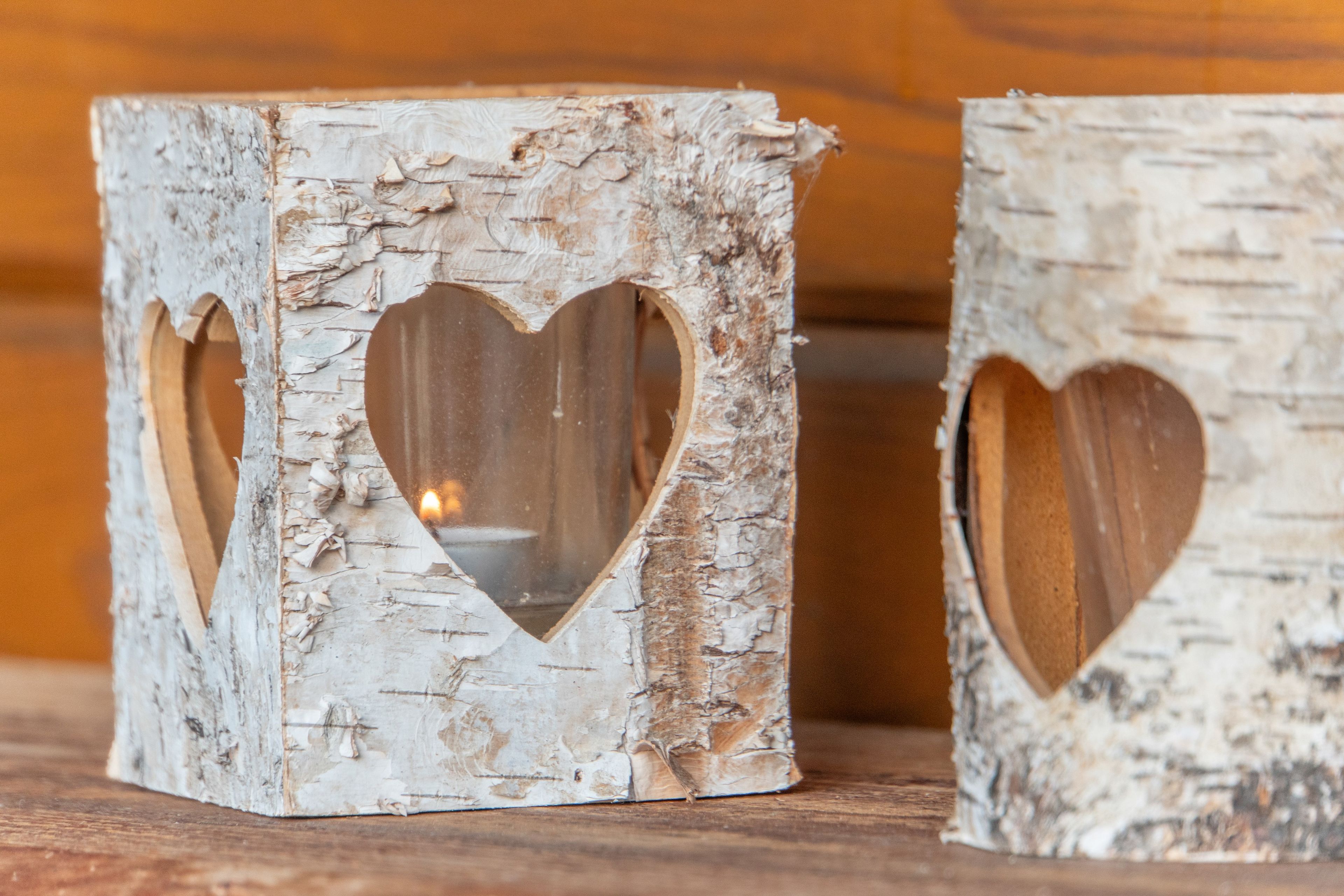 Dos portavelas rústicos de madera con recortes en forma de corazón.
