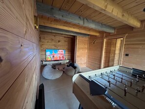 Ein Holzinnenraum mit einem Tischfußballspiel und einem an der Wand befestigten Fernseher.