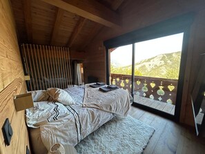Ein Schlafzimmer einer Holzhütte mit einem Bett, einem Nachttisch und einem großen Fenster mit Blick auf eine Berglandschaft.