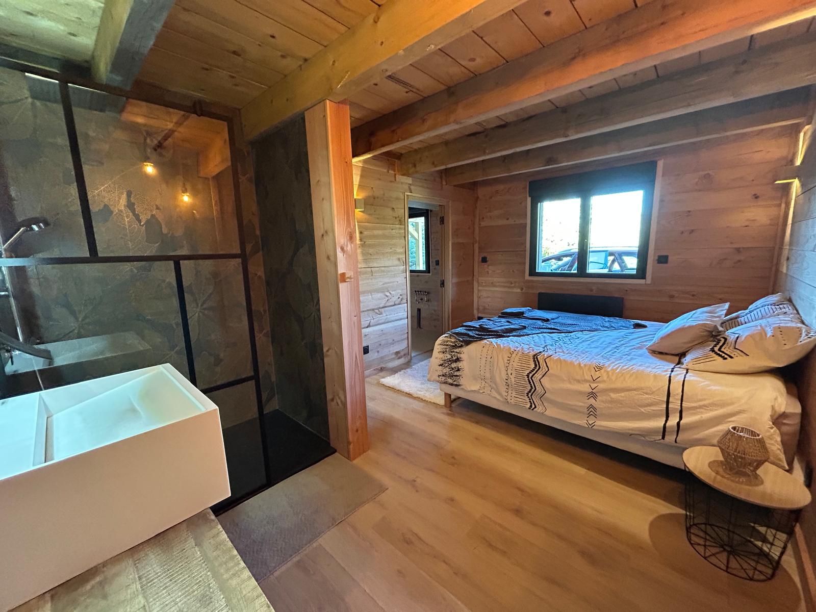Interior de una cabaña de madera con una cama, un baño con lavamanos y una ventana.