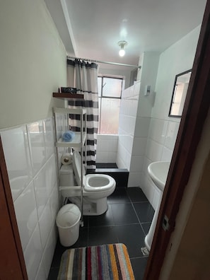 Ein kleines Badezimmer mit Toilette, Waschbecken, Duschbereich und einem Fenster für natürliches Licht.
