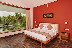 A hotel room with a large window, a bed with white bedding and decorative pillows, a wooden nightstand, and a framed picture on the wall. - Sterling Palavelli Godavari (Elamanchili)