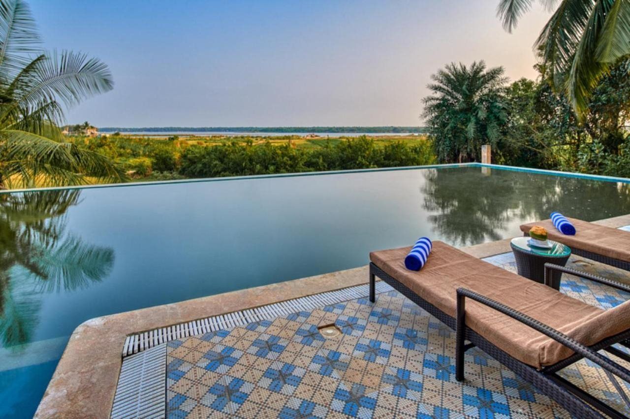 An infinity pool with lounge chairs and a tiled deck, overlooking a landscape with greenery and a distant view.