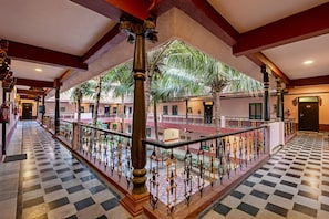 A hotel corridor with checkered flooring, ornate railings, and palm trees.