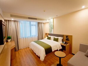 A hotel room with a large bed, a bedside table with a lamp, a small round table, and a sofa. - Greentree Hotel (Fuyang)