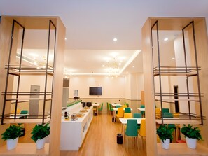 Un comedor moderno con varias mesas y sillas, una barra central con alimentos y un televisor montado en la pared.