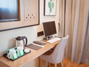 Habitación de hotel con un escritorio de madera, una computadora, una silla, una cafetera y una bandeja con tazas y vasos.