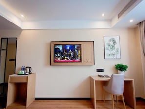 A hotel room with a television mounted on the wall, a desk with a chair, a small table with a kettle, and a framed picture on the wall. - Greentree Hotel (Fuyang)